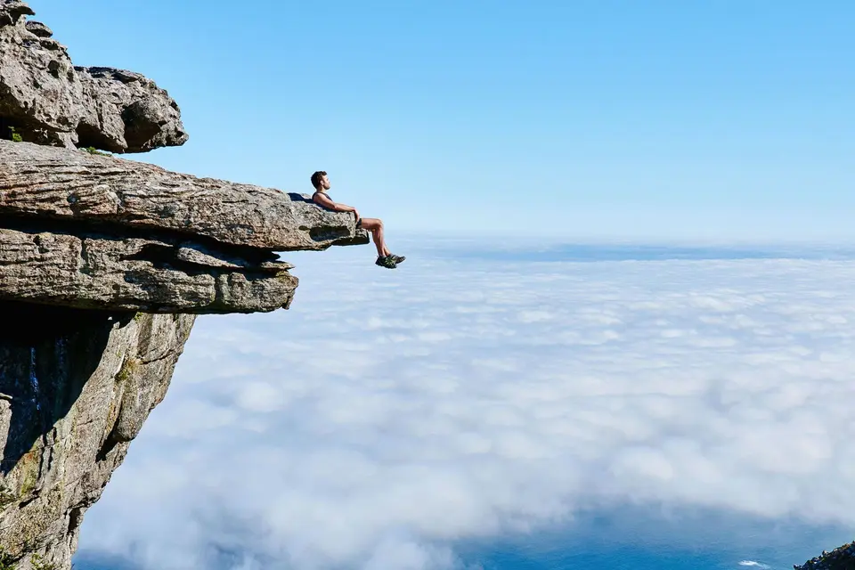Person sitting on a cliff above the ocean