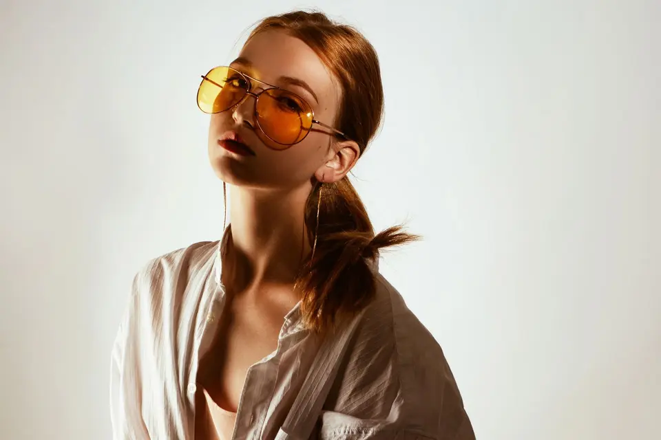 Person in an oversized white shirt and round sunglasses