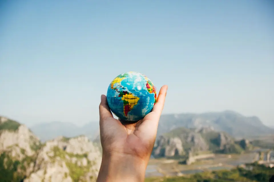 Hand holding a small globe in front of mountains