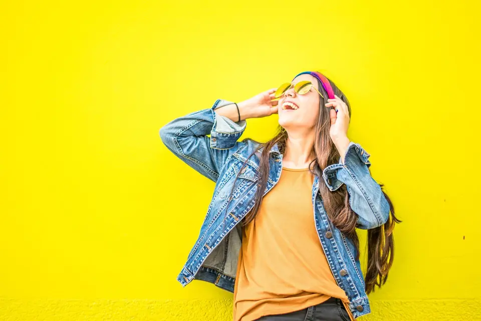 Smiling person in a rust-colored blazer against a yellow wall